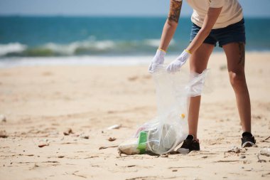 Plajı temizlerken çöp, plastik ve cam şişeleri toplayan kadın gönüllü görüntüsü. Dünya Günü
