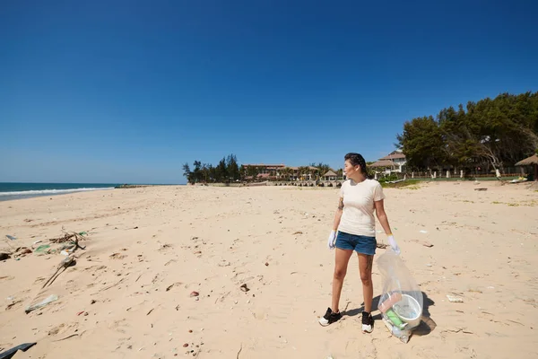 Kobieta Shircie Dżinsowych Spodenkach Spacerując Piaszczystej Plaży Zbierając Śmieci Rozlane — Zdjęcie stockowe