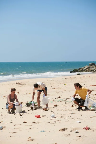 地球の日に砂浜を掃除するときに袋にプラスチックごみを拾うボランティアのグループ — ストック写真