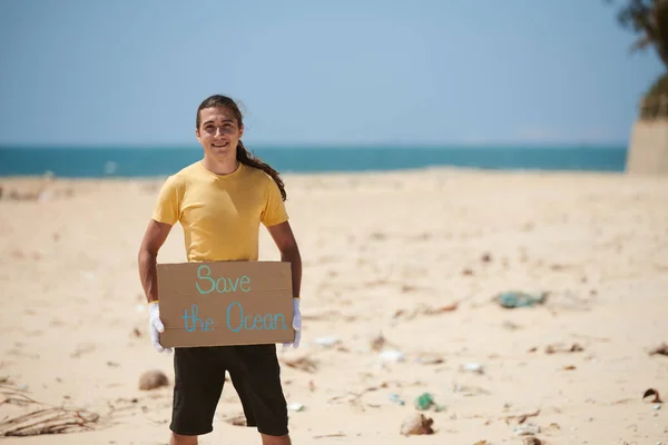 ビーチに立って海のポスターを保持している若い活動家を笑顔 — ストック写真