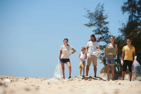 ビーチクリーンアップ後の未来のポスターを保存し 汚れたビーチに立って活動家のグループ 地球の日に — ストック写真