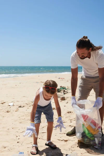 砂のビーチでゴミを収集する父親を助けるとき繊維手袋を身に着けている女の子 — ストック写真