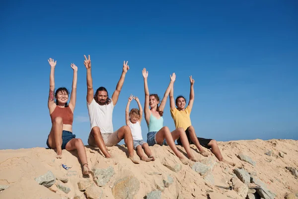 Group Joyful People Sitting Beach Raising Arms Enjoying Sunrays Sea — Stock Photo, Image