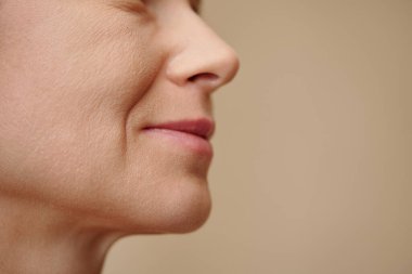 Burun kıvrımlı orta yaşlı bir kadının yüzü, bej renkte izole edilmiş.