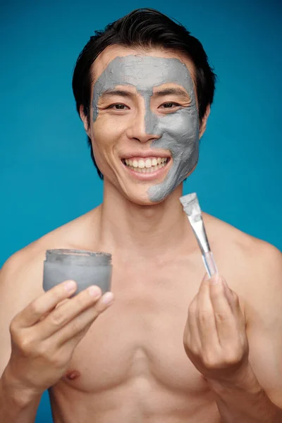 Portrait of excited fit man applying charcoal mask on his face