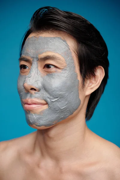 Happy man with exfoliating mask on his face looking away