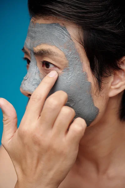 Man checking if clay mask dried on his face and it is time to wash it off