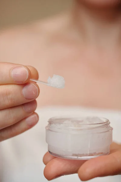 Hands of woman taking exfoliating scrub from jar with small spatula