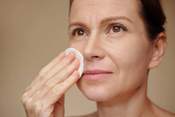 Mature woman wiping face with cotton pad soaked in toner to moisturize skin