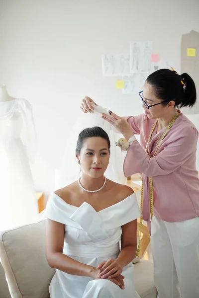 Wedding salon worker helping bride to wear veil