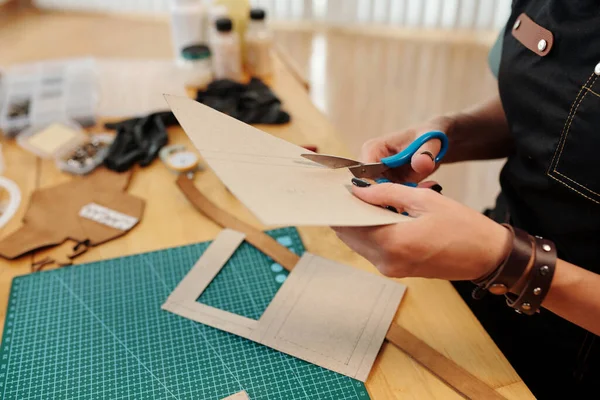 Craft person cutting out cardboard patterns for leather item