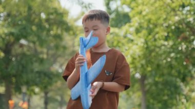 Neşeli, küçük Asyalı çocuğun, oyuncak uçağını havaya fırlatırken ve yaz günü dışarıda oynarken gülümserken, seçici odak çekimini yap.