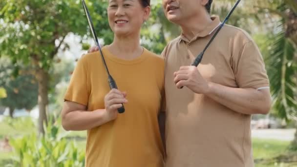 夏の日に公園に屋外に立って成熟したアジアのカップルのショットを傾け 笑顔とバドミントンラケットでカメラにポーズ — ストック動画