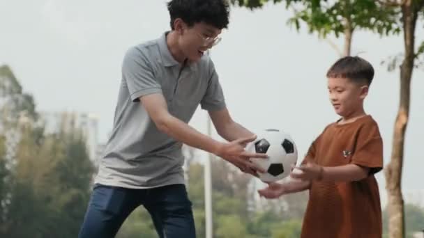 中長いショットのアジアの父教える小さな息子の方法ジャグリングサッカーボール日中公園で — ストック動画
