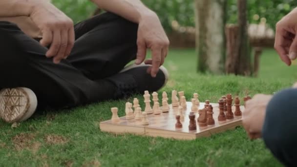 夏の日に公園で緑の芝生の上に座っている間にチェスをしているアジアの男のショットを傾けます — ストック動画