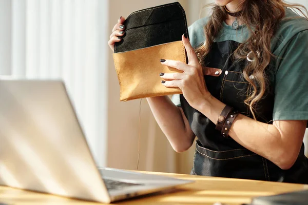 Woman showing almost finished leather bag to customer during online call