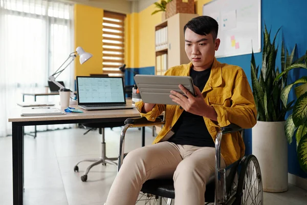 Młody Człowiek Niepełnosprawnością Czytający Artykuł Tablecie Podczas Pracy Biurze — Zdjęcie stockowe