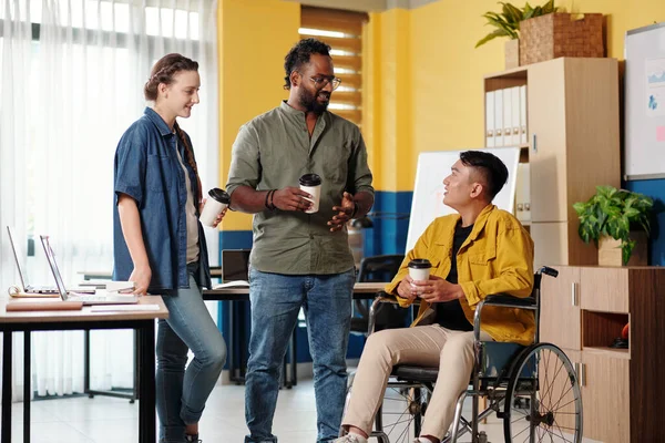 Kahve molası sırasında iş arkadaşlarıyla konuşan engelli genç bir adam.