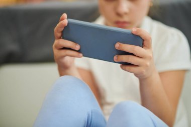 Oyun oynarken veya kısa videolar izlerken mobil uygulama kullanan küçük bir kızın kırpılmış görüntüsü