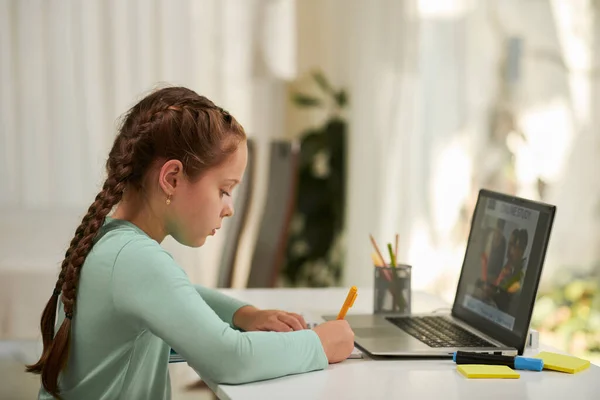 女子高生は学校のプラットフォーム上で教育ビデオを見ているときに教科書にメモを取る — ストック写真