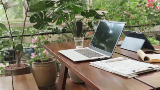 有笔记本电脑 数码平板电脑 商业用纸和水杯 装饰着绿色植物的咖啡店的中景餐桌 那里没有人 — 图库视频影像
