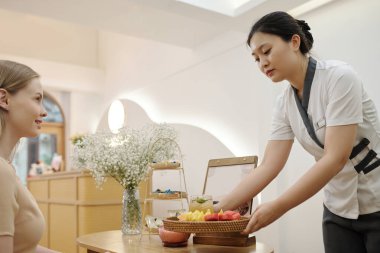 Güzellik salonu resepsiyonisti müşteriye taze meyve ve buzlu çay getiriyor.