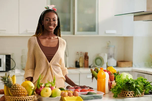 一个面带微笑的年轻黑人妇女站在厨房柜台旁拿着新鲜食品的画像 — 图库照片