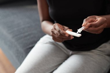 Evdeki koronavirüs enfeksiyonunu tespit etmek için antijen test kiti kullanan bir kadının yakın çekim görüntüsü.