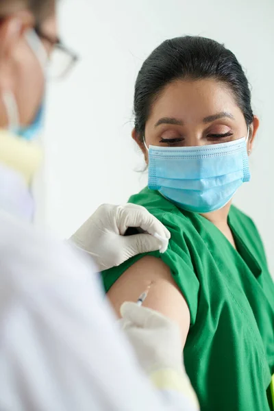 医者を見て保護マスクの看護師彼女の肩の中にコロナウイルスに対してワクチンを注射 — ストック写真