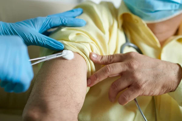コロナウイルスに対する予防接種の前に綿球で患者の腕の上に注射部位を拭く看護師 — ストック写真