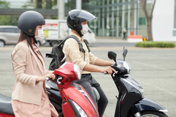 Young people wearing protective helmets and medical masks when riding to work on scooters