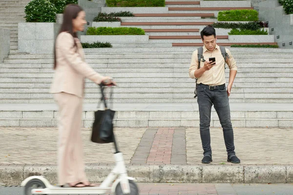 Poważny Młody Człowiek Stojący Chodniku Czytający Sms Smartfonie Gdy Kobieta — Zdjęcie stockowe