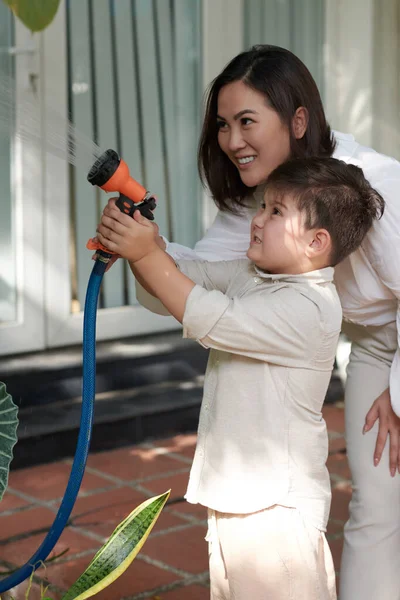 Uśmiechnięta Matka Wyjaśniająca Synowi Jak Używać Węża Ogrodowego Roślin Wodnych — Zdjęcie stockowe