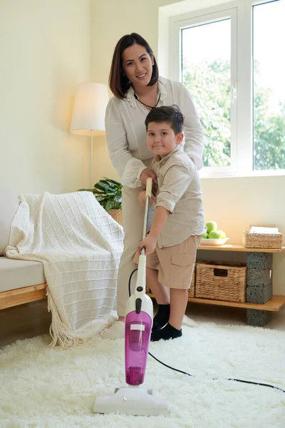 微笑的母亲教小儿子如何吸尘干净的毛毯 — 图库照片