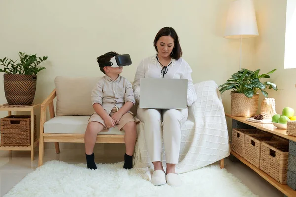小さな男の子で仮想現実の眼鏡遊びビデオゲーム彼の母親によって胸 — ストック写真