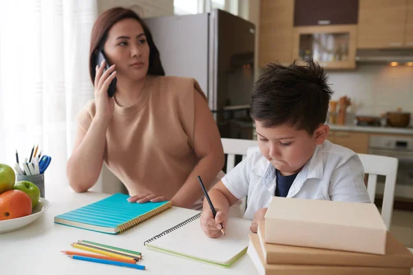 Schooljongen Doet Huiswerk Onder Controle Van Zijn Moeder Praten Telefoon — Stockfoto