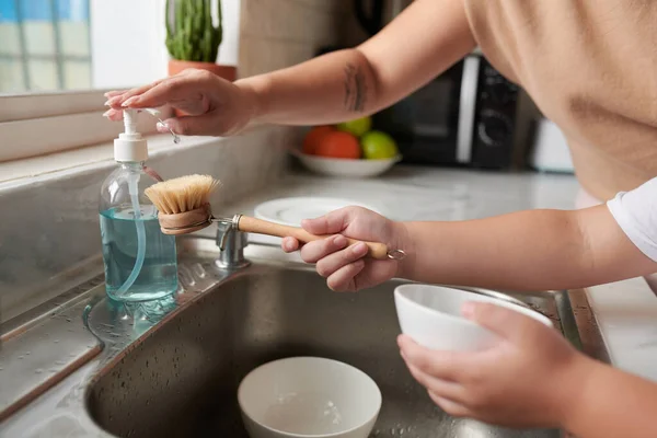 Руки Матери Помогают Сыну Добавлять Моющее Средство Мытья Посуды Щетку — стоковое фото