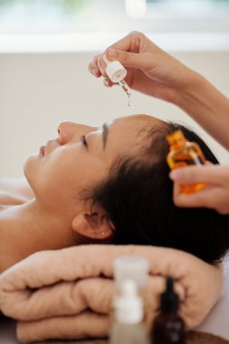 Güzellik uzmanının, genç bir kadının yüzüne yaşlanma önleyici serum sürerken damlatıcı kullandığı yakın plan görüntüsü.