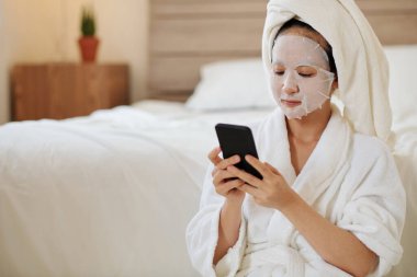 Yüzünde çarşaf maskesi olan ciddi bir genç kadın sabah duşundan sonra arkadaşlarına mesaj atıyor.