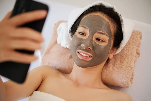 Glimlachende Jonge Vrouw Met Klei Masker Gezicht Ontspannen Bed Spa — Stockfoto