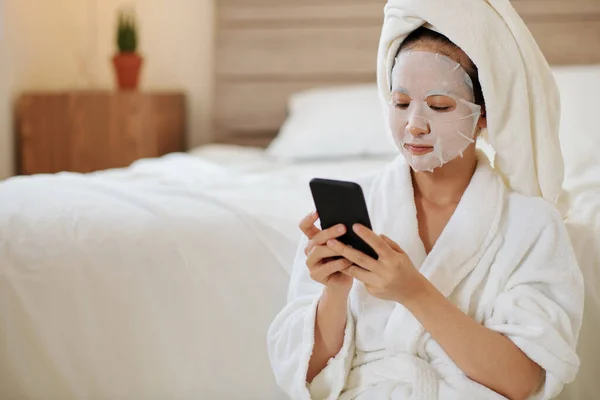 Poważna Młoda Kobieta Maską Twarzy Smsowanie Znajomych Porannym Prysznicu — Zdjęcie stockowe