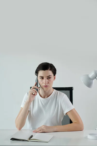 深刻な若いビジネスマン女性がオープンプランナーとデスクに座って同僚と電話で話す — ストック写真