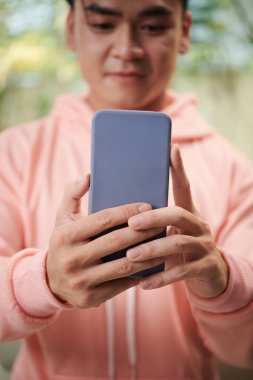 Pembe kapüşonlu genç adam sosyal medya hesabı için akıllı telefondan selfie çekiyor.