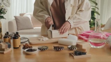 Tanımlanamayan bir kadının el yapımı sabun tabanını atölyedeki ahşap masada parçalara ayırdığı görüntüler.