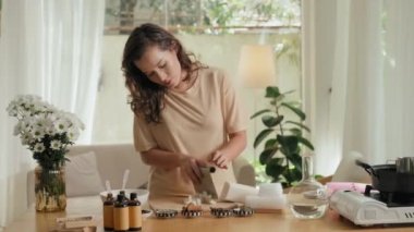 Kafkasyalı genç bir kadının, ahşap masadaki vazoda bir buket güzel beyaz kasımpatı ile el yapımı sabun yaptığı orta boy bir fotoğraf.