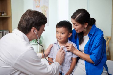 Çocuk doktoru, annesi ona sarıldığında küçük çocuğun nefesini dinliyor.