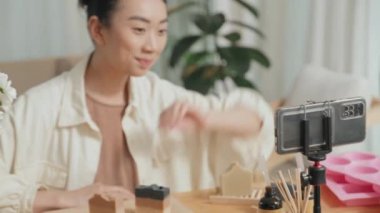 Genç, güzel Asyalı bir kadın akıllı telefondan video tarifi kaydediyor. Estetik atölyesinde ahşap masada oturuyor.