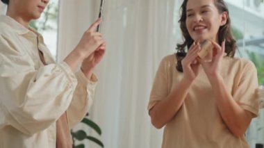 Asyalı bayan arkadaşı akıllı telefondan video kaydederken, beyaz bir kadının organik kozmetik ürünler sergilediği orta boy bir fotoğraf.