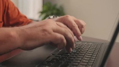 Dizüstü bilgisayarda yazı yazan ve evde çevrimiçi çalışırken defterine not alan tanınmayan kıdemli bir adamın el resimleri.