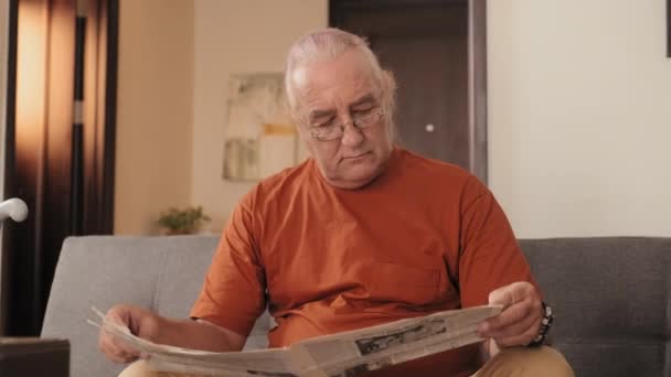 Mediana Toma Anciano Gafas Leyendo Periódico Mientras Está Sentado Sofá — Vídeo de stock
